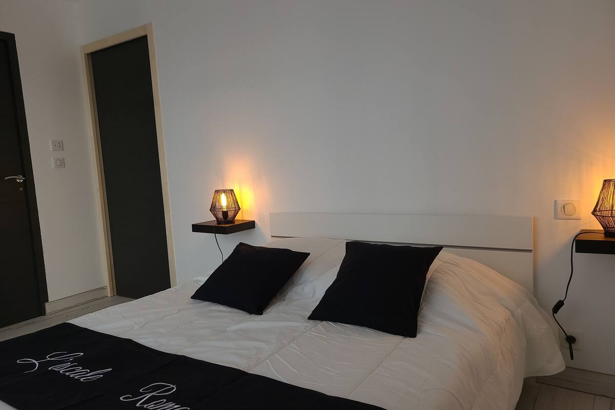 A neatly made bed with a black and white bedspread, two black pillows, and a bedside table with a lamp.