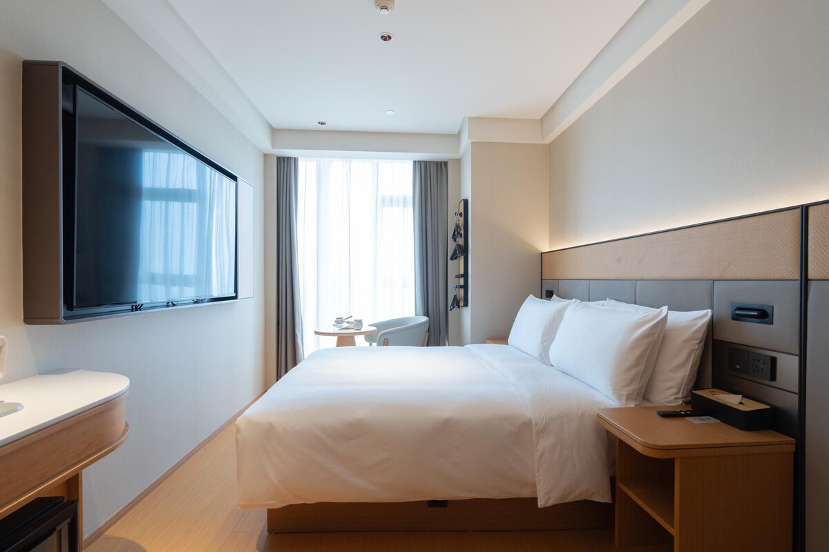 A hotel room with a bed, bedside table, TV, and a desk with a chair.