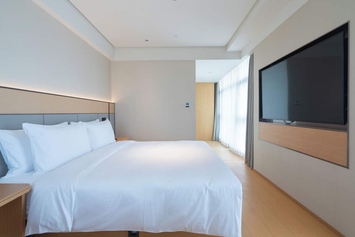 Una habitación de hotel moderna con una cama grande, un televisor de pantalla plana montado en la pared y vistas al exterior a través de amplios ventanales.