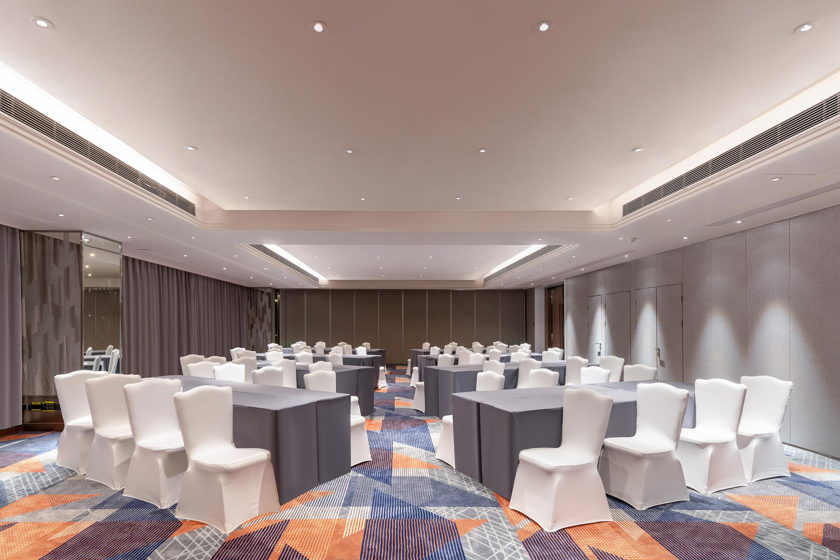 A conference room with rows of tables and chairs, a patterned carpet, and a modern ceiling design.