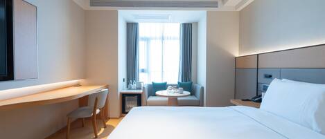 Een hotelkamer met een groot bed, een bureau met stoel, een kleine tafel met stoel, en een aan de muur bevestigde televisie.