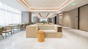 A modern, well-lit lounge area with seating and tables, a central sofa, and a wooden stool. - Ji Hotel Guangzhou Tianhe Sports Center (Guangzhou)