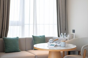 A modern living room with a round table, beige sofa, and a view of the outdoors through large windows. - Ji Hotel Guangzhou Tianhe Sports Center (Guangzhou)