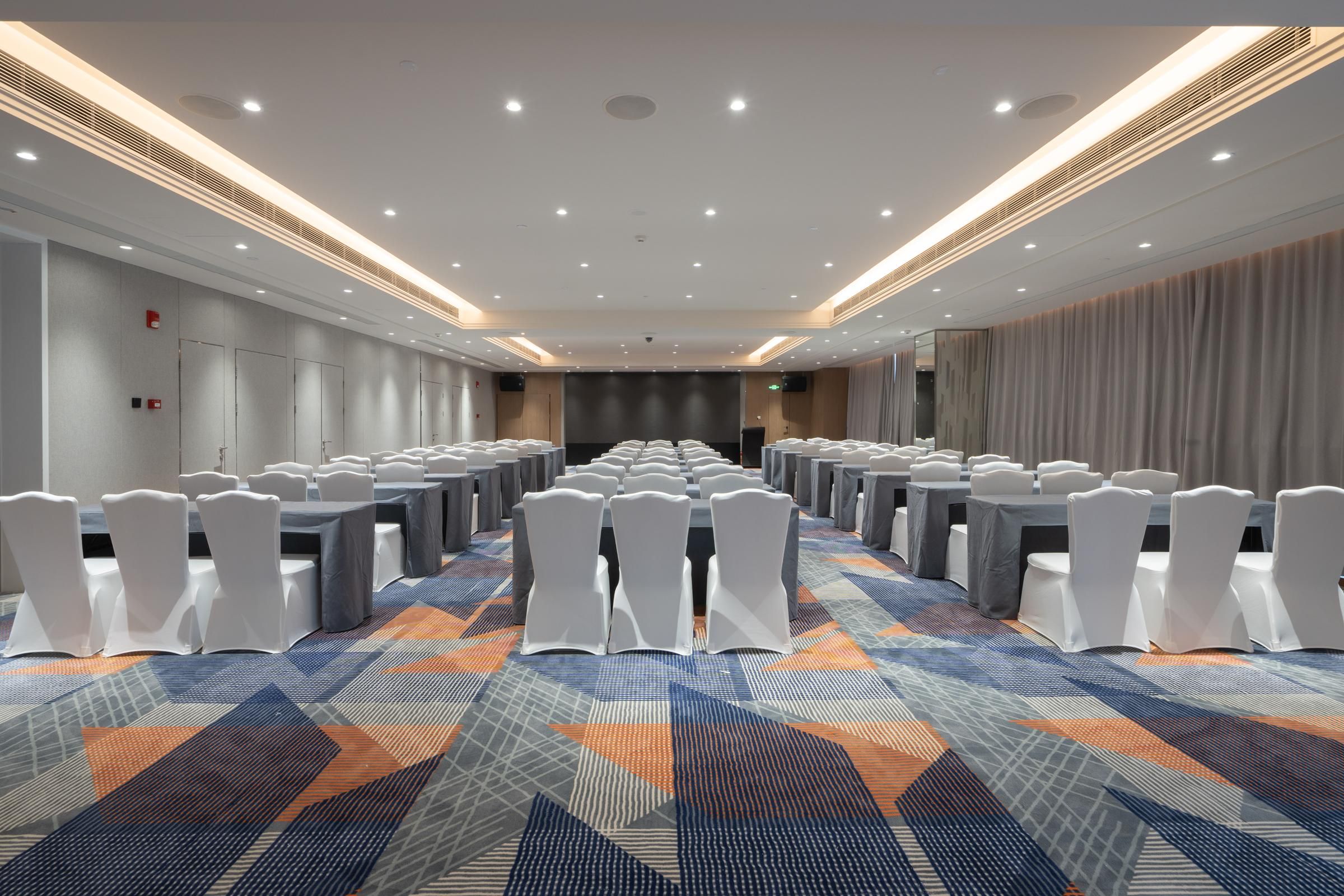 A conference room with rows of tables and chairs, a patterned carpet, and a modern ceiling design.