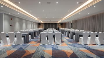 A conference room with rows of tables and chairs, a patterned carpet, and a modern ceiling design.