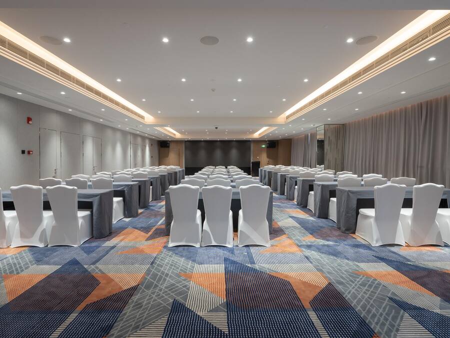 A conference room with rows of tables and chairs, a patterned carpet, and a modern ceiling design.