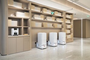 A modern hotel lobby with a clean, minimalist design, featuring a large bookshelf, a coffee machine, and three self-service kiosks. - Ji Hotel Guangzhou Tianhe Sports Center (Guangzhou)