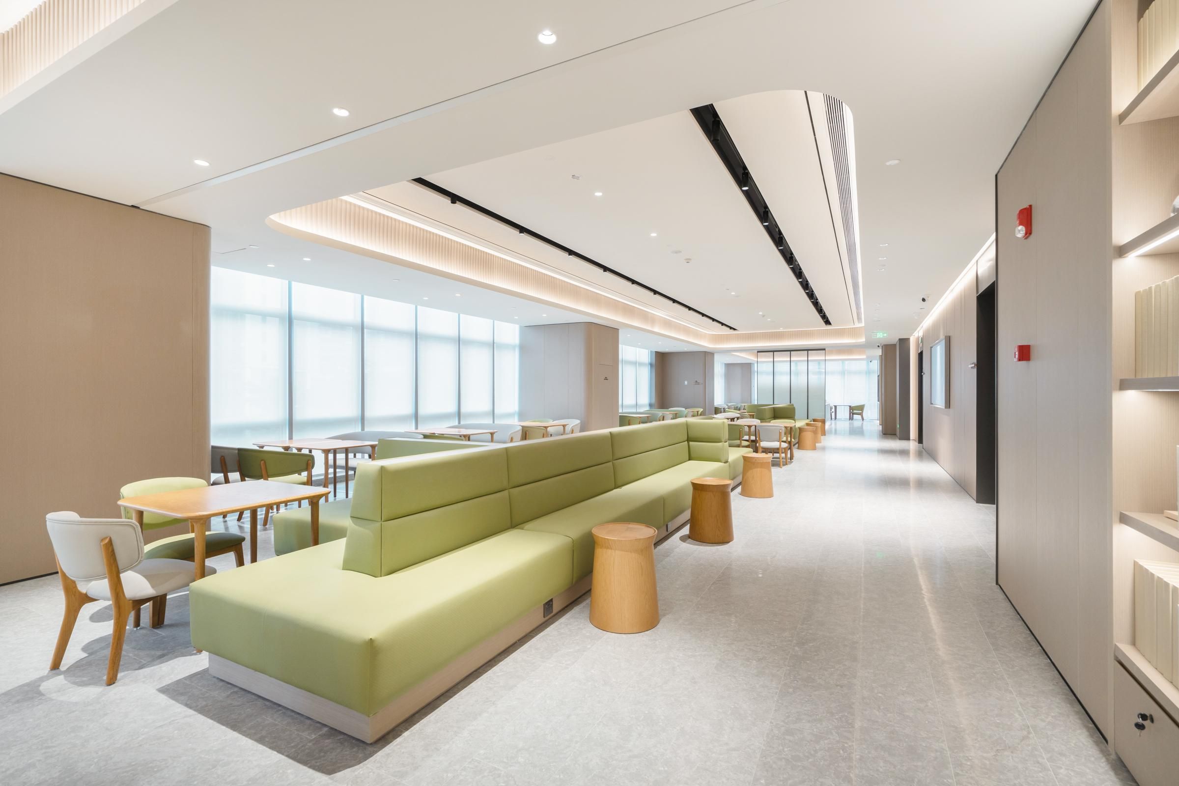 A modern hotel lobby with a green seating area, wooden tables, and a spacious layout.