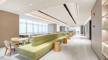 A modern hotel lobby with a green seating area, wooden tables, and a spacious layout.