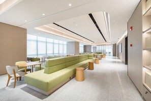 Un moderno vestíbulo de hotel con un área de estar verde, mesas de madera y un diseño espacioso.