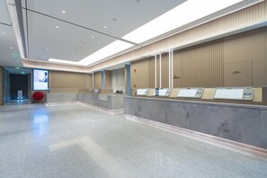 A modern reception area with a marble floor, a large screen displaying a video, and a row of self-service kiosks. - Ji Hotel Guangzhou Tianhe Sports Center (Guangzhou)