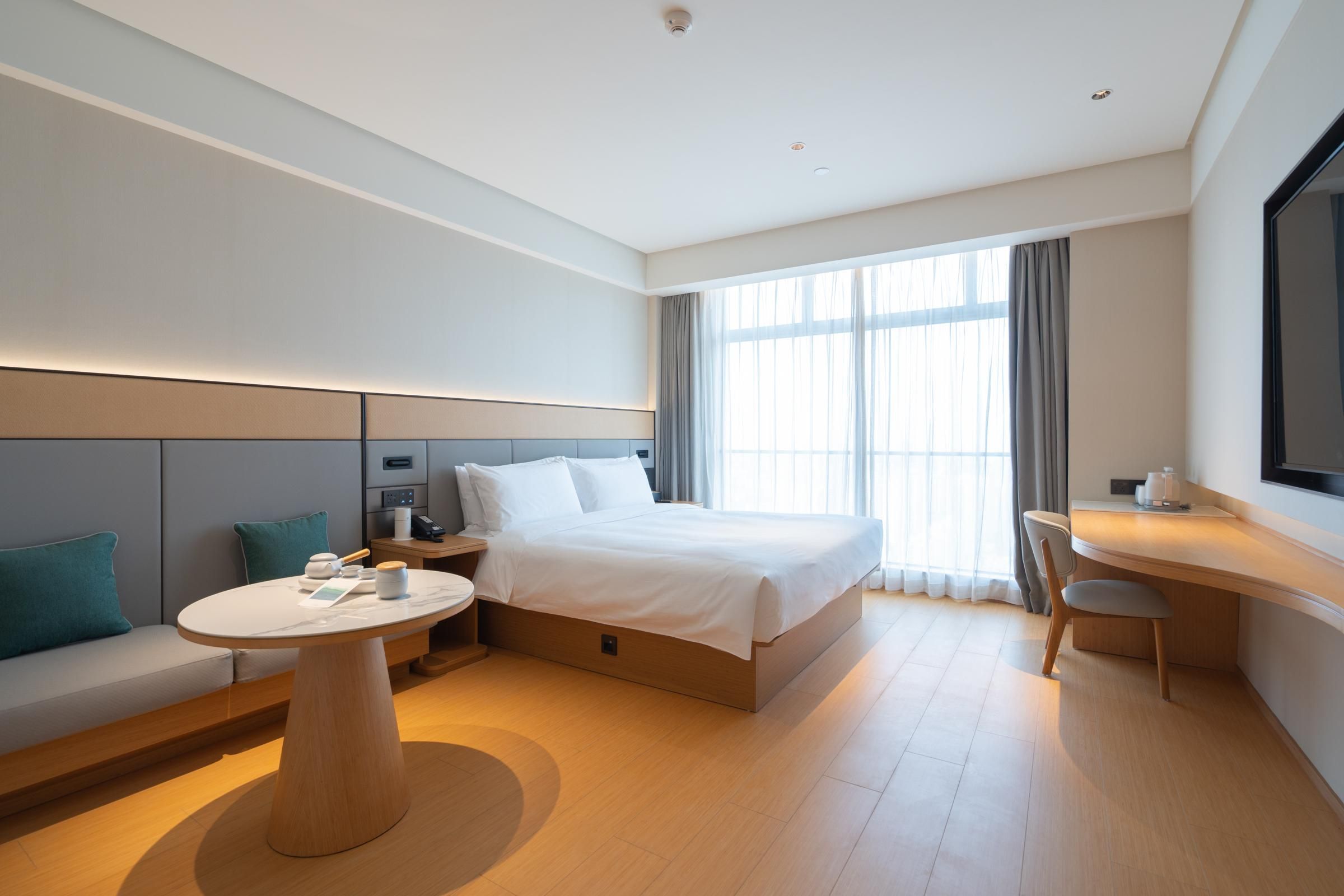 A modern hotel room with a bed, a round table, a sofa, and a desk.