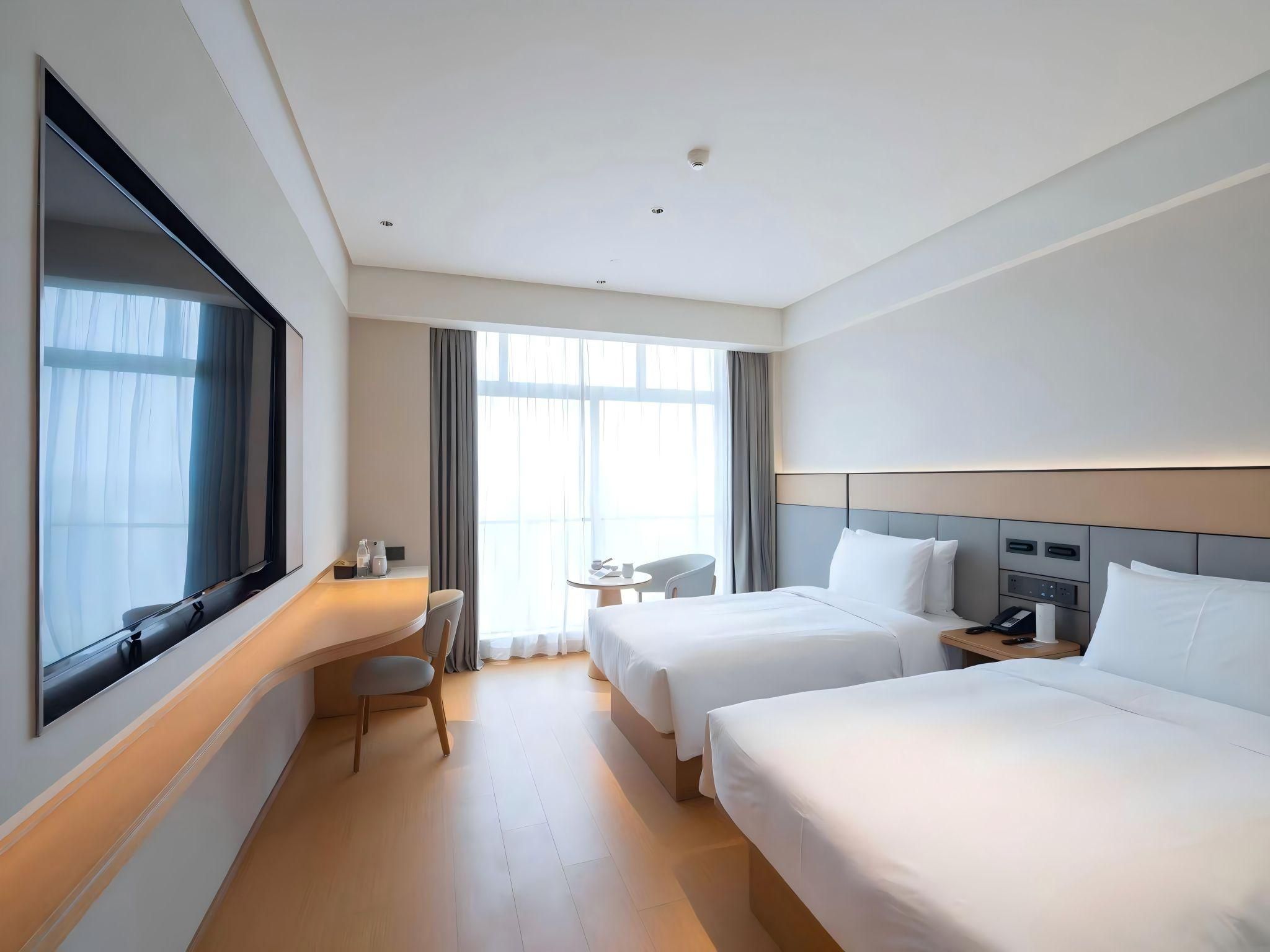 A hotel room with two beds, a desk, a chair, and a large window.