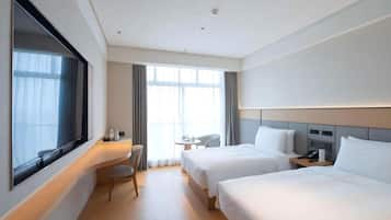 A hotel room with two beds, a desk, a chair, and a large window.