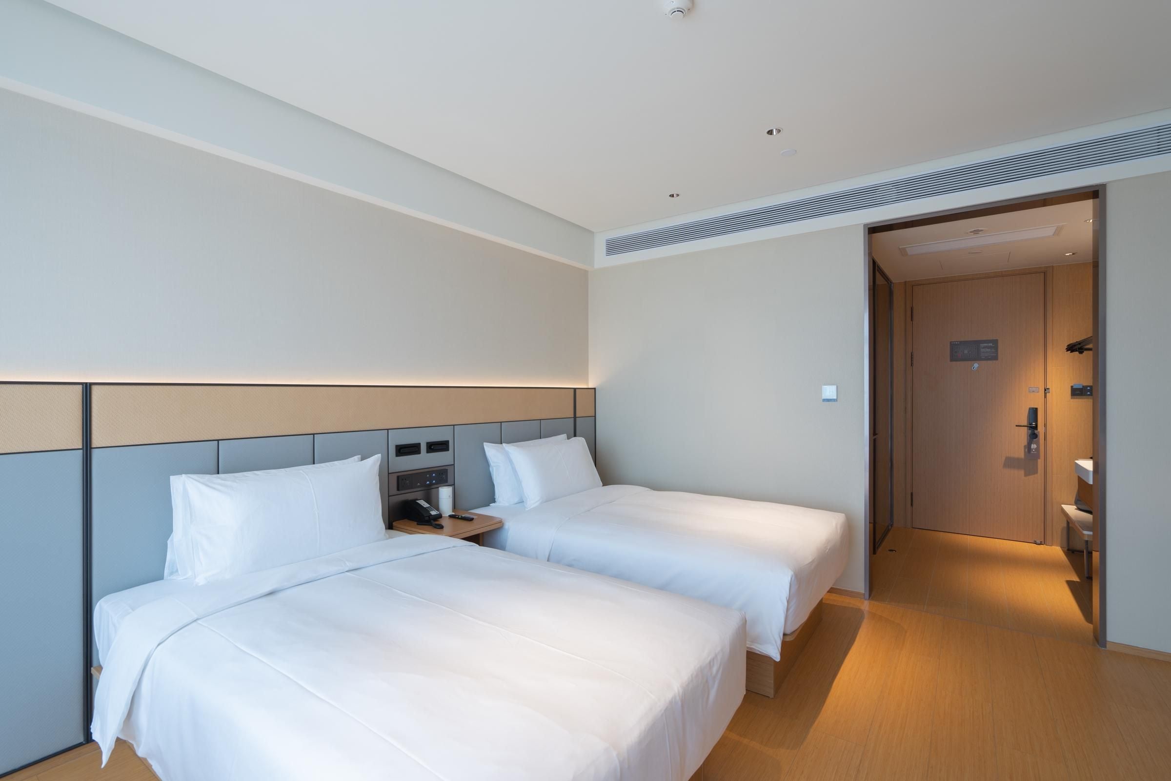 A hotel room with two beds, a bedside table with a phone, and a door leading to a bathroom.