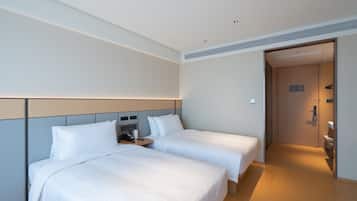 A hotel room with two beds, a bedside table with a phone, and a door leading to a bathroom.