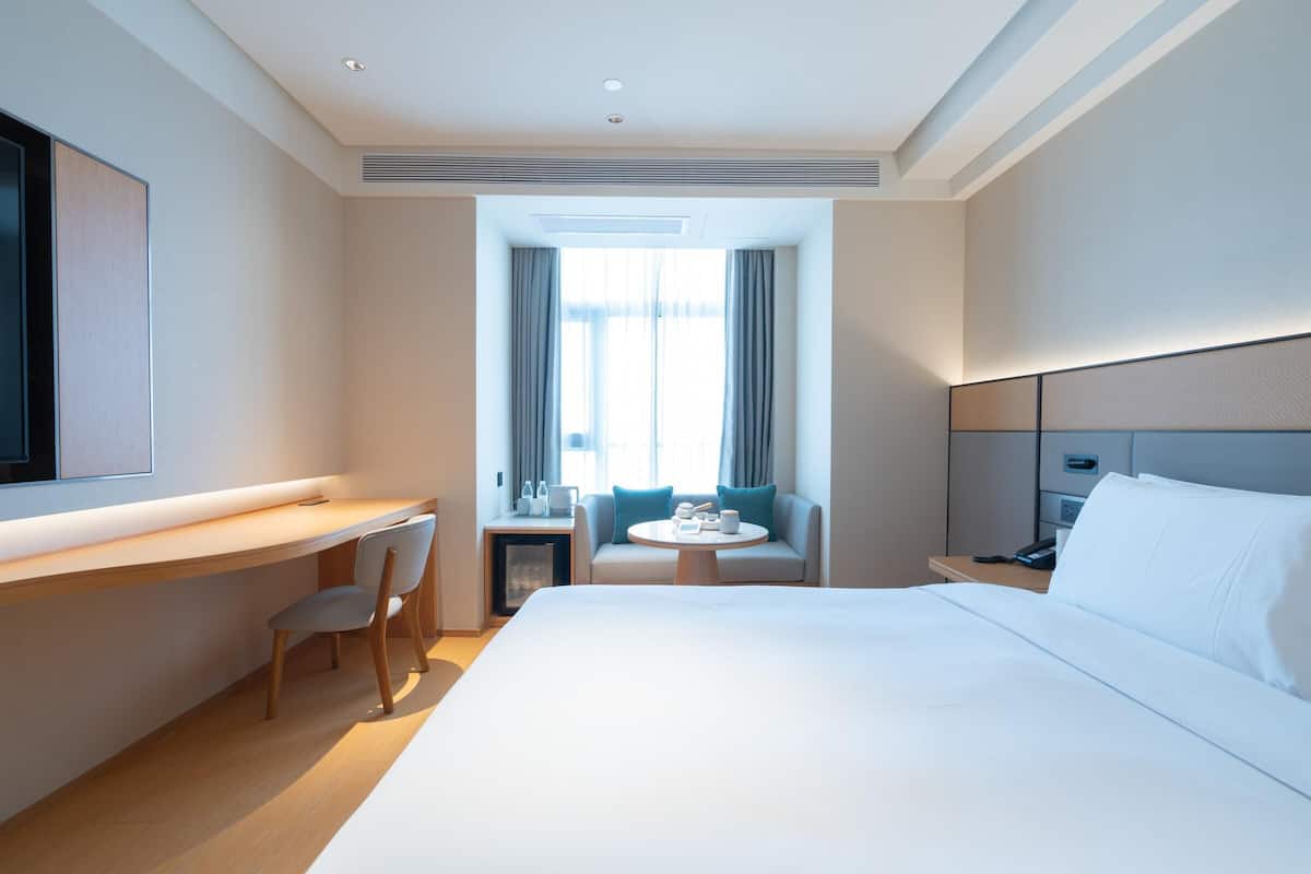 Una habitación de hotel con una cama grande, un escritorio con silla, una mesita con otra silla y un televisor fijado a la pared.