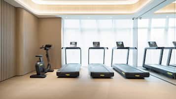 A modern gym with four treadmills aligned in a row, a stationary bike, and a wall-mounted exercise bike.