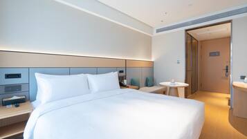 A modern hotel room with a large bed, bedside tables, a small round table, and a separate bathroom area.