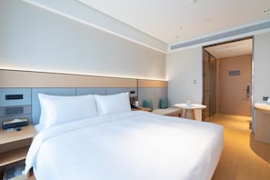 Una habitación de hotel moderna con una cama grande, mesitas de noche, una pequeña mesa redonda y un baño separado.