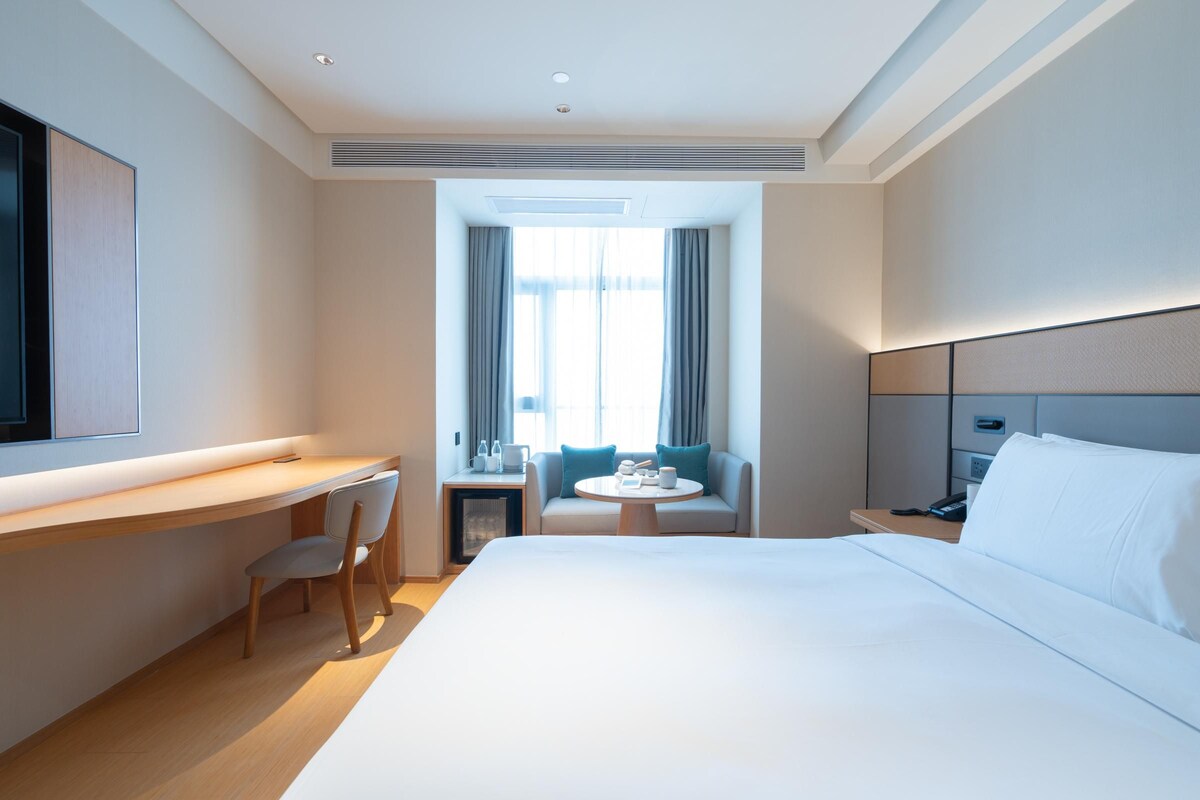 A hotel room with a large bed, a desk with a chair, a small table with a chair, and a TV mounted on the wall.