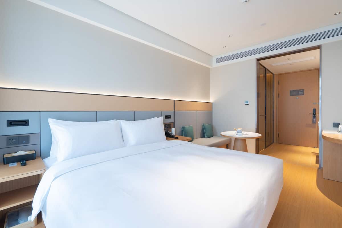 Una habitación de hotel moderna con una cama grande, mesitas de noche, una pequeña mesa redonda y un baño separado.