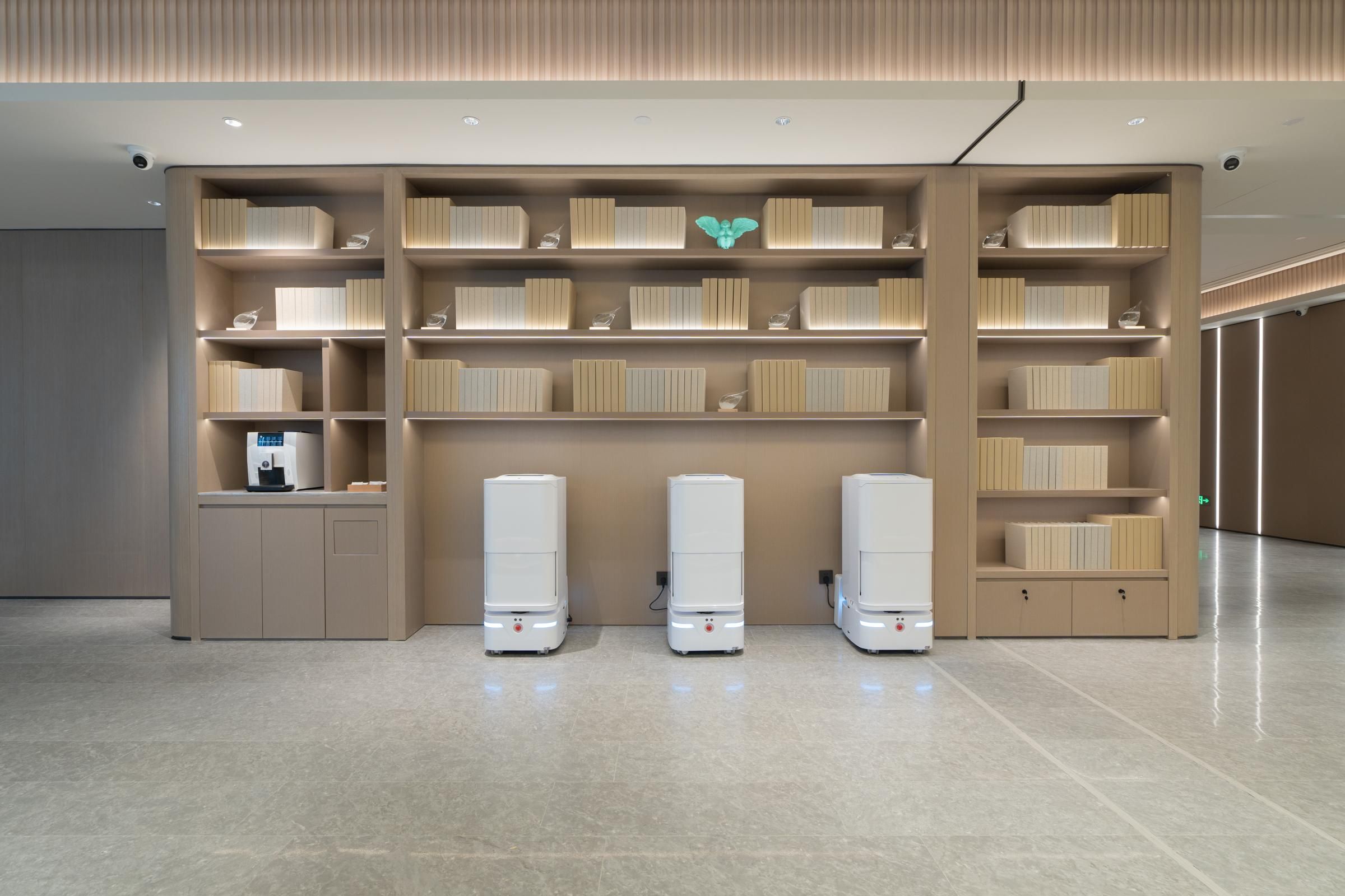 A modern interior with a central bookshelf, a coffee machine, and three white vending machines.