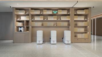 A modern interior with a central bookshelf, a coffee machine, and three white vending machines.