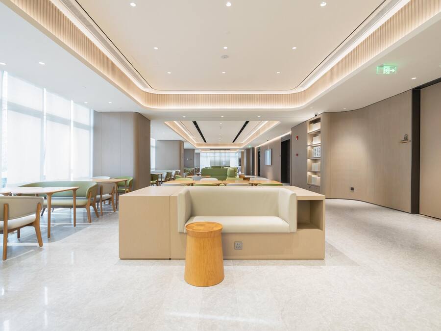 A modern, well-lit lounge area with seating and tables, a central sofa, and a wooden stool.