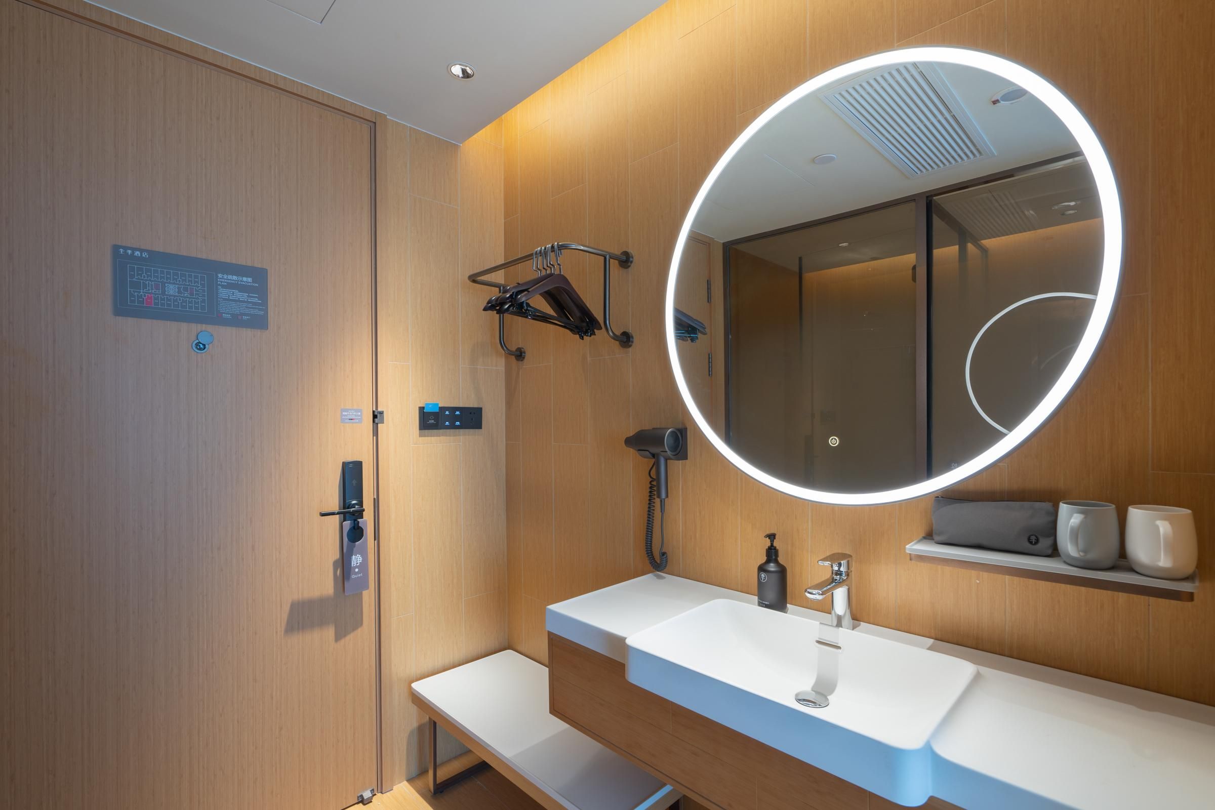 Un baño moderno con pared de madera, un espejo redondo con luz, un lavabo y un perchero para toallas.