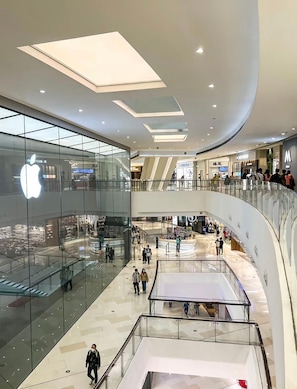 Un centro comercial de varios niveles con escaparates de vidrio, incluyendo una tienda Apple, y un espacio central abierto con barandilla de vidrio.