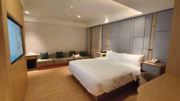 Una habitación de hotel moderna con una cama grande, una zona de estar con un sofá y sillones, un escritorio con teléfono, y un televisor en la pared.