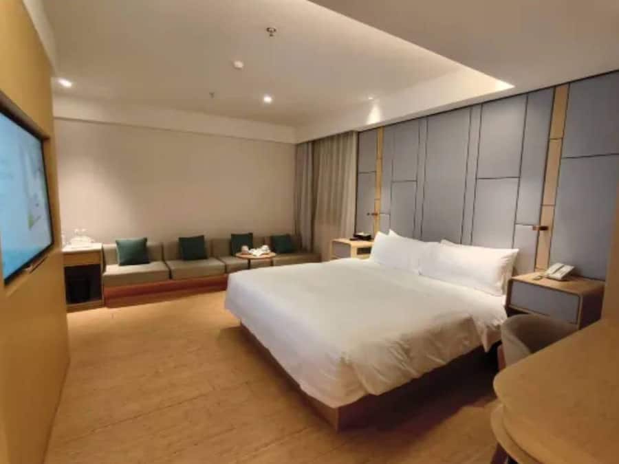 Una habitación de hotel moderna con una cama grande, una zona de estar con un sofá y sillones, un escritorio con teléfono, y un televisor en la pared.