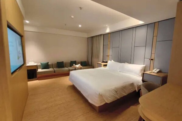 A modern hotel room with a large bed, a seating area with a sofa and chairs, a desk with a phone, and a TV on the wall. - Ji Hotel Guangzhou Tianhe Sports Center (Guangzhou)