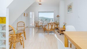 A spacious loft with a high ceiling, a dining area with wicker chairs, a wooden table, and a view of the city through large windows. - Prisange by Interhome (Roses)