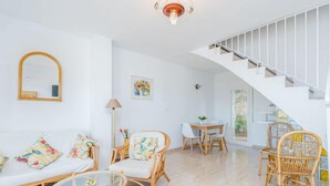 A spacious living area with a white staircase, wicker furniture, and a glass coffee table. - Prisange by Interhome (Roses)