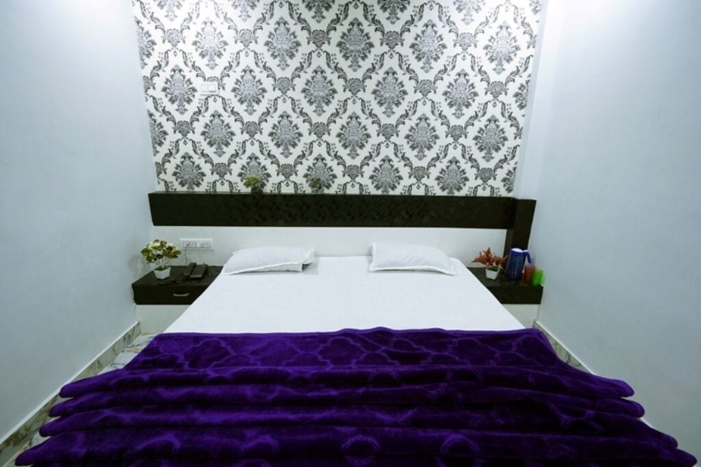 A neatly made bed with a purple blanket, a black headboard, and a patterned wallpaper.