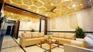 A modern living room with a sectional sofa, a coffee table, and a ceiling with hexagonal lighting. - Hotel Alishaan (Ajmer)