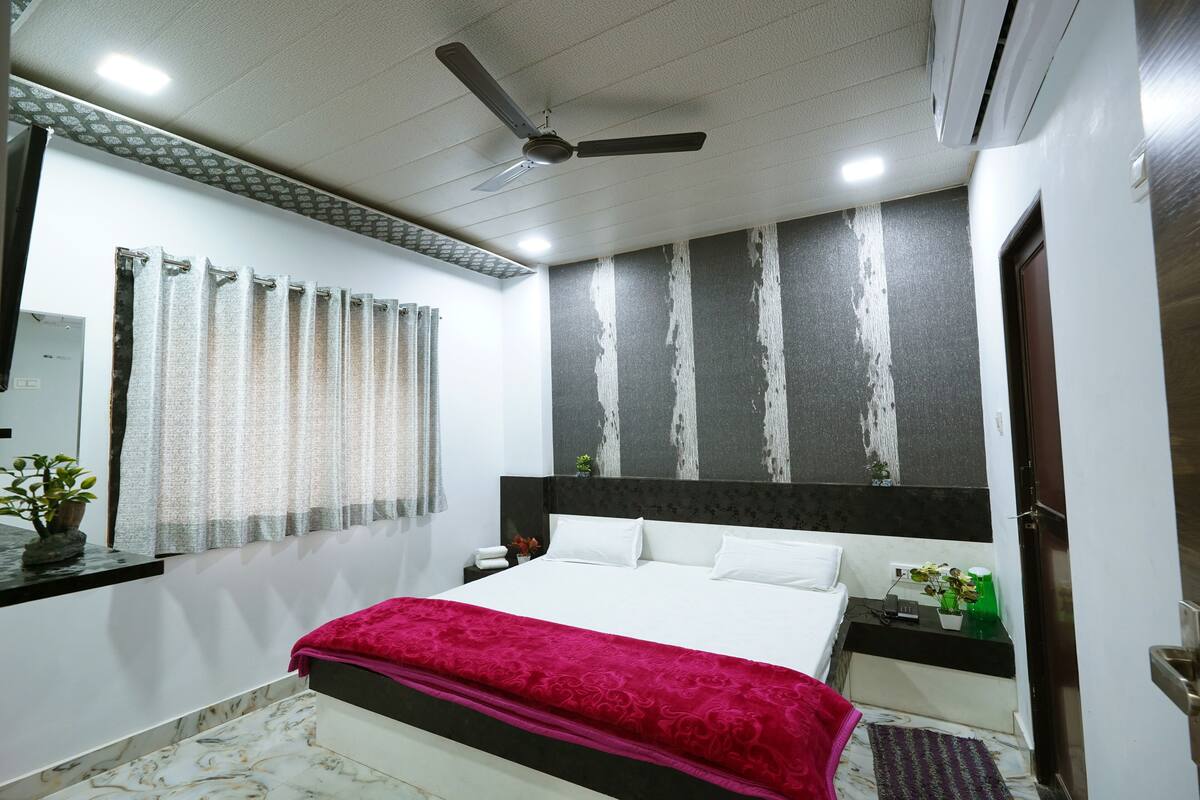 Un dormitorio con cama, mesita de noche, ventilador de techo, ventana con cortinas y pared con diseño texturizado.