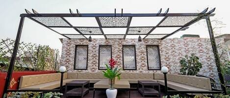 A covered outdoor seating area with a patterned wall and a pergola overhead.