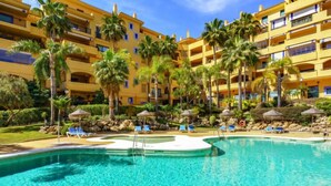 A resort with a large pool surrounded by palm trees and sun loungers.