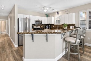 A spacious kitchen with white cabinets, a granite countertop, and a central island with bar stools.