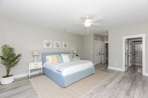 Une chambre à coucher avec un lit, des tables de chevet, un ventilateur de plafond et une plante en pot.