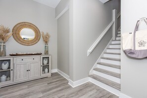 A hallway with a wooden floor, a white staircase, a grey wall, a wooden cabinet with drawers, and a mirror with a wooden frame.