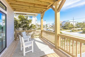 Terraza de madera con dos sillas blancas y un tapete, con vista a un barrio residencial con casas y árboles.
