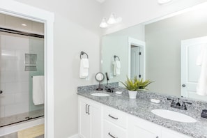 Une salle de bain moderne avec deux lavabos, un grand miroir et une douche à parois de verre.