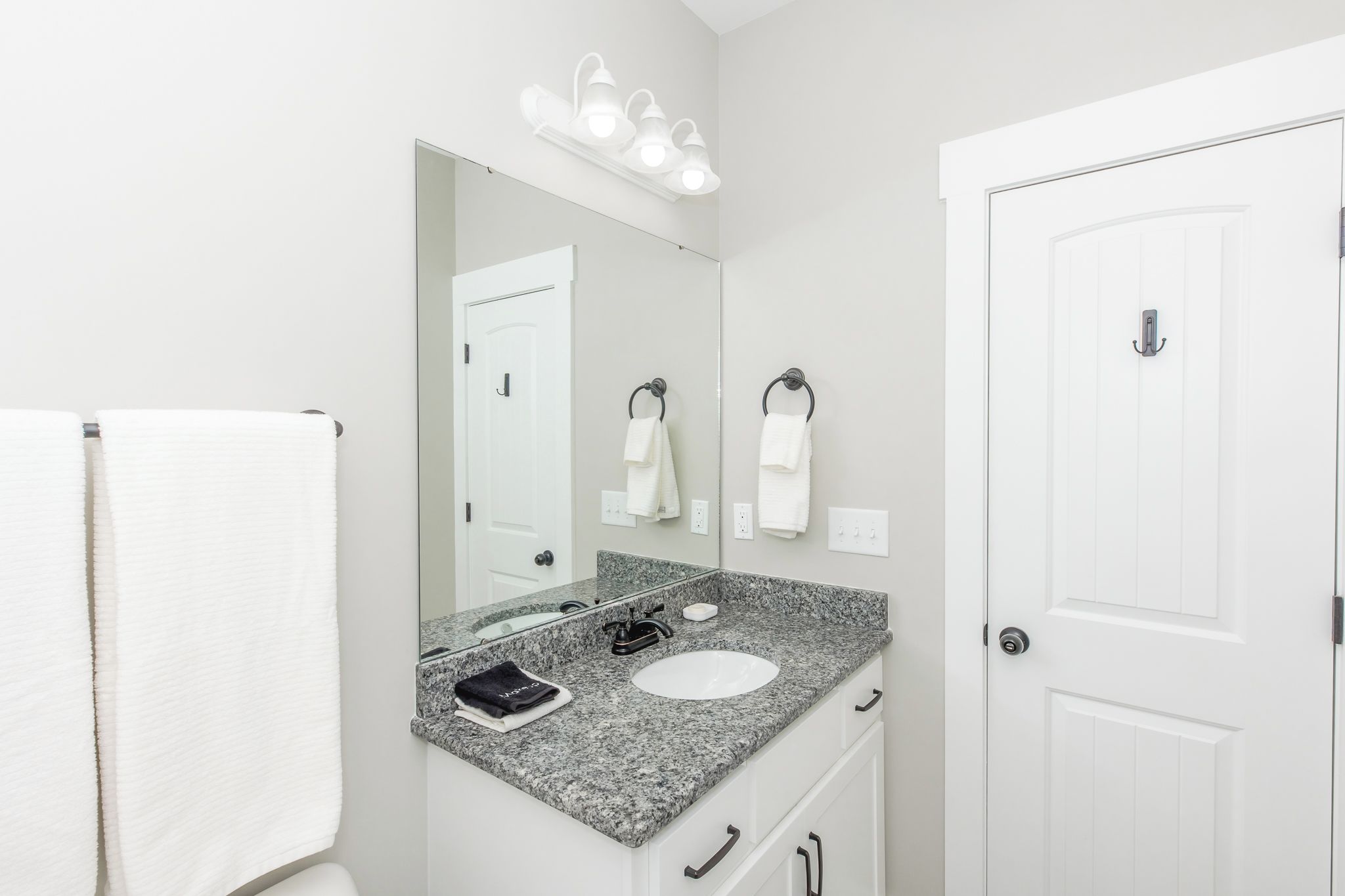 A bathroom with a granite countertop, a white sink, a mirror, and a door with a towel rack.