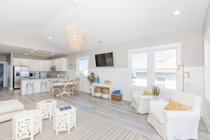 Une cuisine moderne avec des meubles blancs, un coin repas avec une table et des chaises blanches, et un salon avec des canapés blancs et un tapis à motifs.
