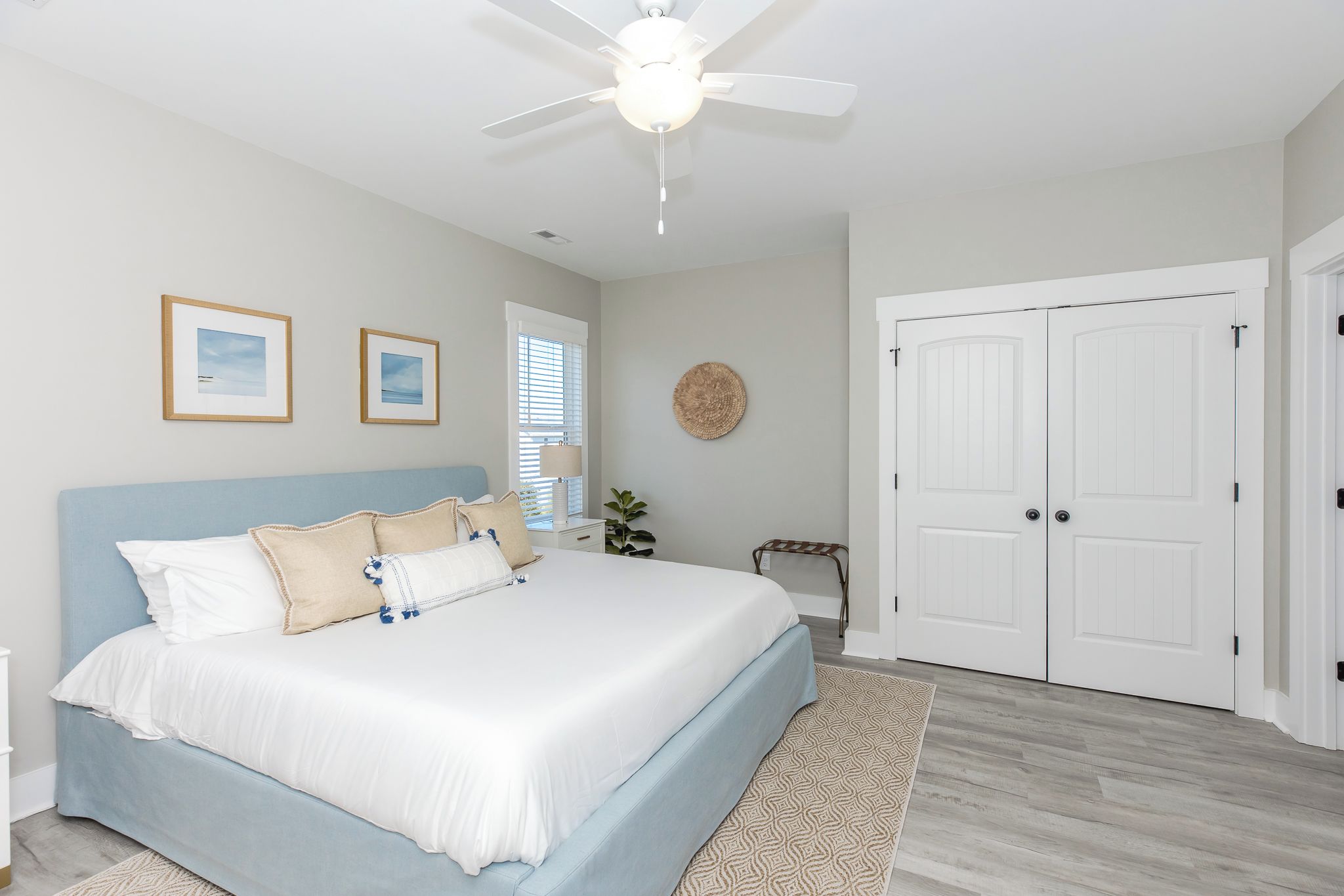 A bedroom with a bed, a ceiling fan, a door, and a window with blinds.