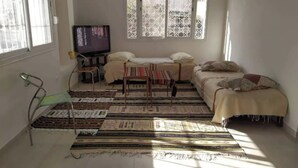 A small, sunlit room with a bed, a TV, and a window with patterned curtains. - Great studio in El-Biar (Algiers)